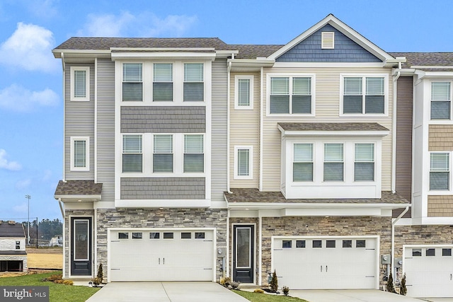 townhome / multi-family property with a garage, stone siding, and concrete driveway