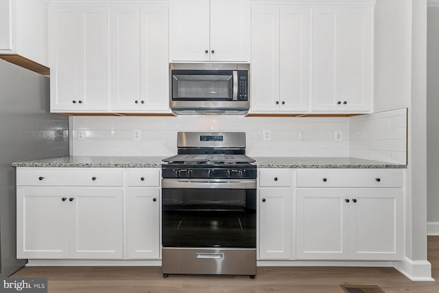 kitchen with light wood finished floors, white cabinets, light stone countertops, and stainless steel appliances