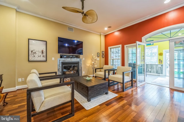 living room featuring visible vents, wood finished floors, ornamental molding, and a glass covered fireplace