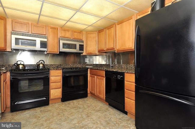 kitchen with dark stone counters, a sink, a paneled ceiling, and black appliances