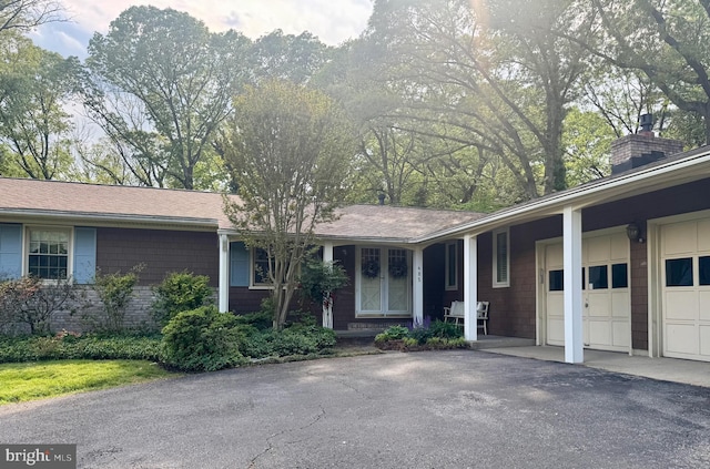 single story home with an attached garage, aphalt driveway, and a chimney