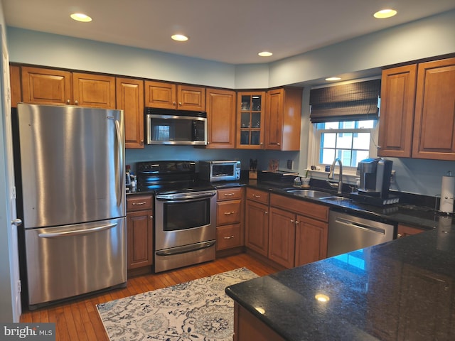 kitchen with brown cabinetry, a sink, dark stone counters, and stainless steel appliances