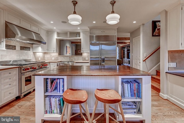 kitchen with butcher block counters, light wood-style floors, wall chimney range hood, high quality appliances, and a center island