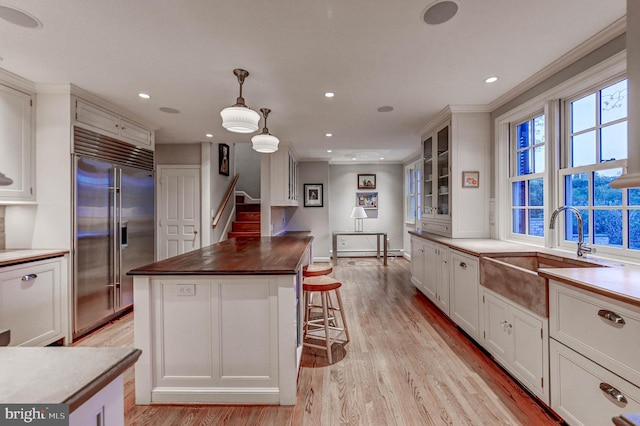 kitchen with glass insert cabinets, white cabinetry, built in fridge, a sink, and light wood-style flooring