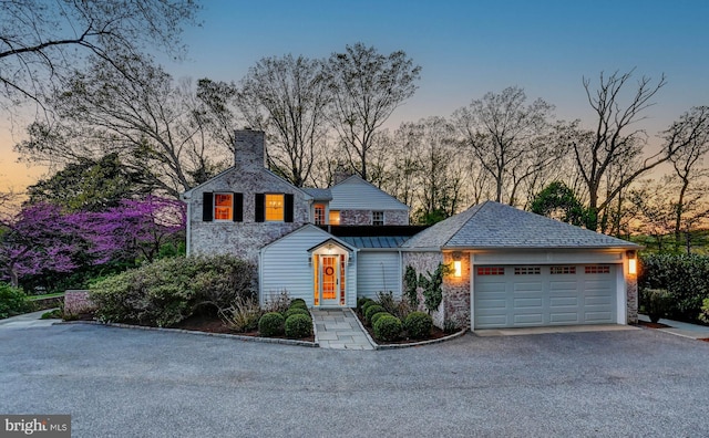 view of front of house featuring an attached garage, stone siding, a chimney, a standing seam roof, and driveway