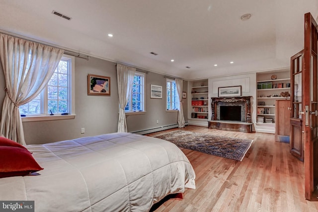 bedroom with a fireplace with raised hearth, a baseboard heating unit, wood finished floors, and visible vents