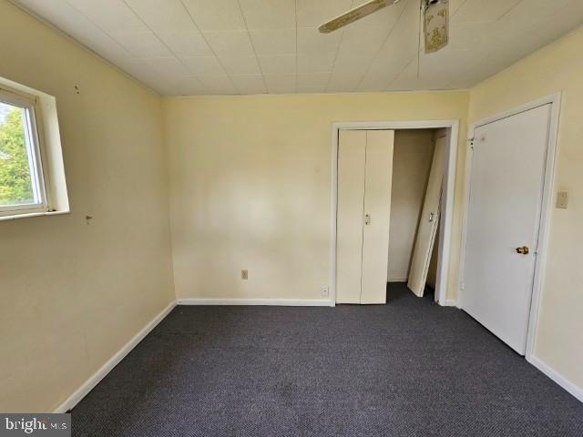 unfurnished bedroom featuring a ceiling fan, baseboards, and dark colored carpet