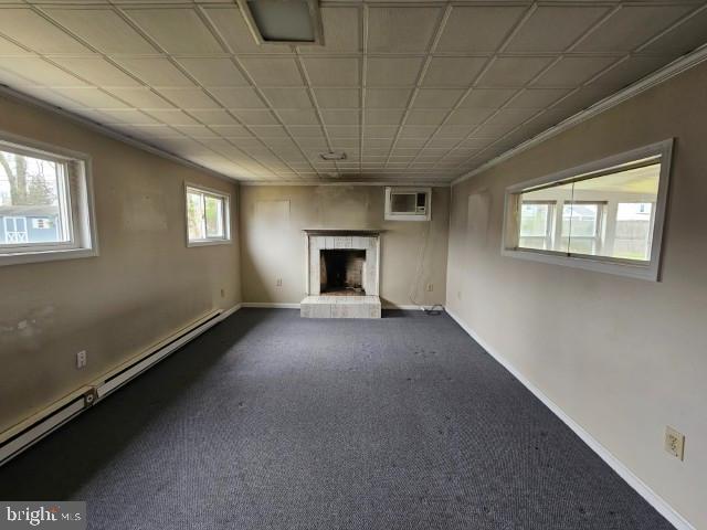 unfurnished living room with crown molding, a fireplace with raised hearth, dark carpet, baseboards, and a baseboard radiator