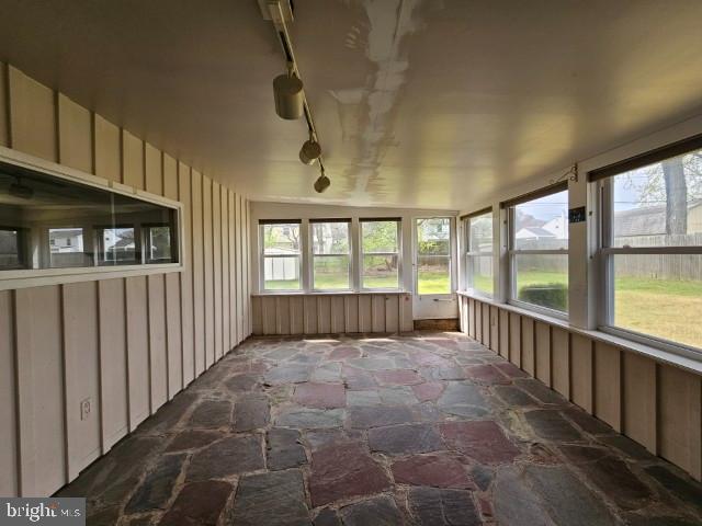 unfurnished sunroom with rail lighting and stone flooring