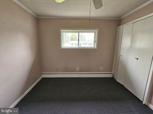 unfurnished bedroom with dark colored carpet, baseboards, crown molding, and a baseboard heating unit