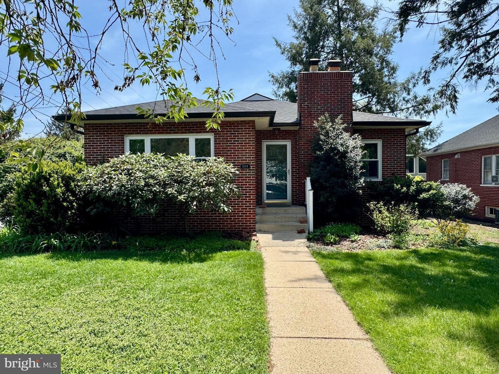 bungalow with a chimney, a front lawn, and brick siding
