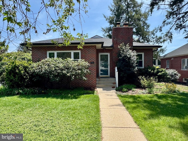 bungalow with a chimney, a front lawn, and brick siding