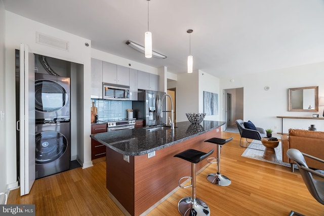 kitchen with visible vents, a breakfast bar, light wood-style floors, stacked washer / drying machine, and stainless steel appliances