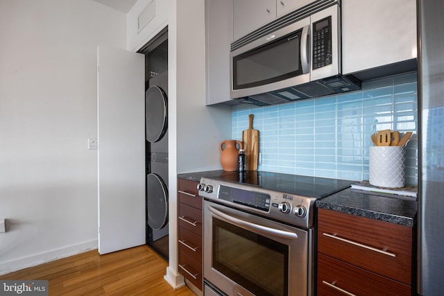 kitchen featuring dark countertops, stainless steel appliances, light wood-type flooring, and stacked washer / dryer