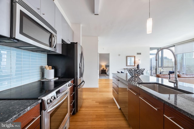kitchen featuring pendant lighting, appliances with stainless steel finishes, tasteful backsplash, light wood-type flooring, and a sink