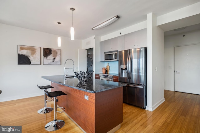kitchen with stacked washer / dryer, a breakfast bar, a sink, light wood-style flooring, and stainless steel appliances