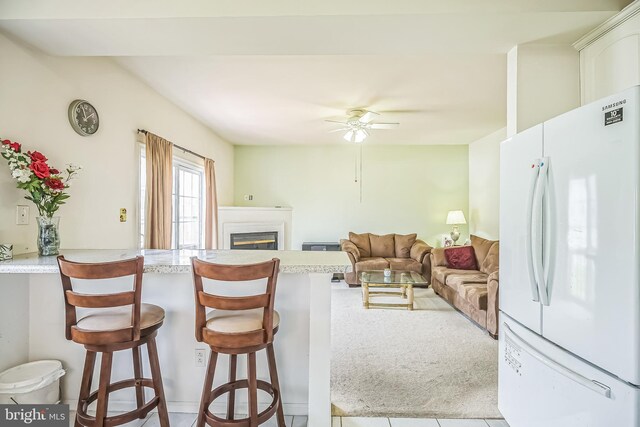 living room featuring light tile patterned floors, a glass covered fireplace, ceiling fan, and light colored carpet