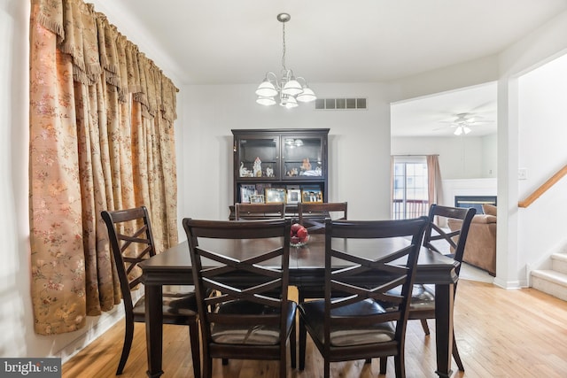 dining room with visible vents, ceiling fan with notable chandelier, stairway, and hardwood / wood-style flooring