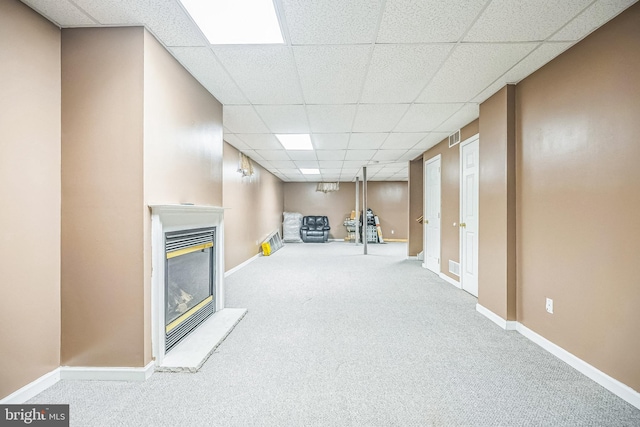 finished basement featuring a paneled ceiling, carpet flooring, a glass covered fireplace, and baseboards
