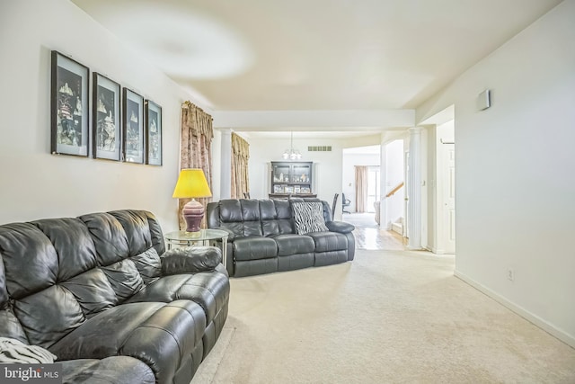 carpeted living area featuring baseboards, a chandelier, visible vents, and decorative columns
