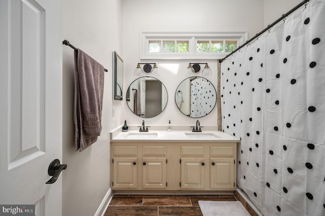 full bath featuring baseboards, double vanity, wood finish floors, and a sink