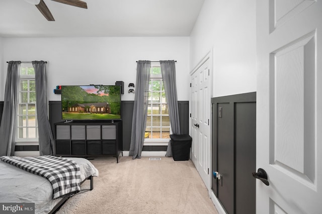 carpeted bedroom with ceiling fan, visible vents, and a wainscoted wall
