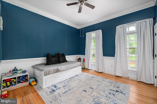bedroom with a ceiling fan, ornamental molding, wood finished floors, and a wainscoted wall