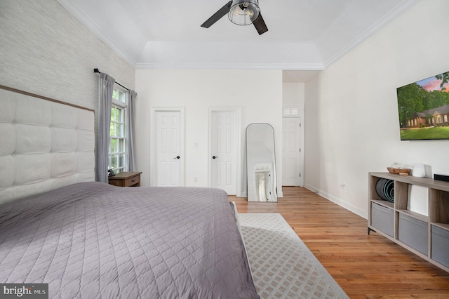 bedroom featuring crown molding, ceiling fan, baseboards, wood finished floors, and a tray ceiling