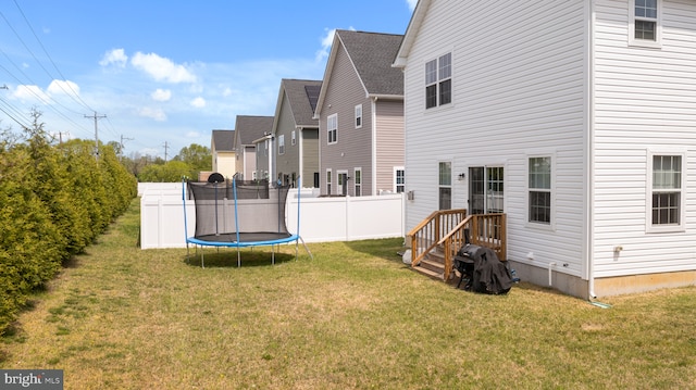 back of house featuring a lawn, fence, and a trampoline