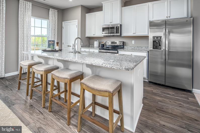 kitchen with a kitchen island with sink, dark wood finished floors, a sink, white cabinets, and stainless steel appliances