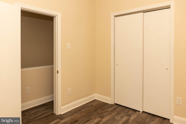 unfurnished bedroom with dark wood-style floors, a closet, and baseboards