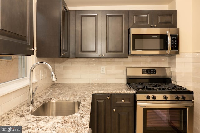 kitchen featuring appliances with stainless steel finishes, a sink, dark brown cabinets, and light stone counters