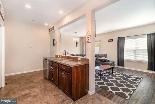 kitchen featuring stainless steel dishwasher, dark countertops, baseboards, open floor plan, and a sink