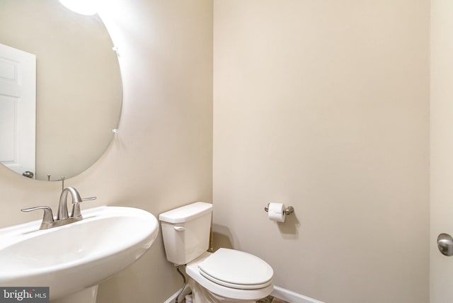 half bathroom featuring baseboards, a sink, and toilet