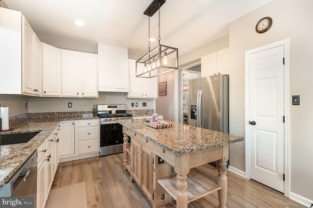 kitchen with a kitchen island, white cabinets, light stone counters, light wood-style flooring, and appliances with stainless steel finishes