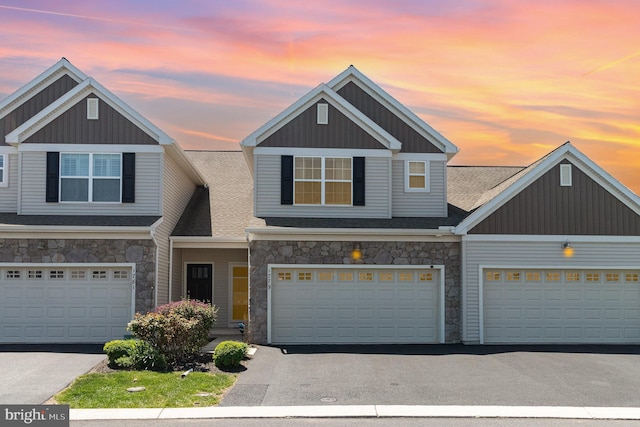 view of property featuring a shingled roof, aphalt driveway, a garage, stone siding, and board and batten siding
