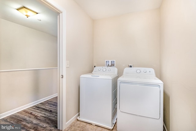 clothes washing area with laundry area, baseboards, wood finished floors, and separate washer and dryer