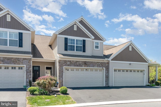 townhome / multi-family property featuring board and batten siding, roof with shingles, stone siding, and aphalt driveway