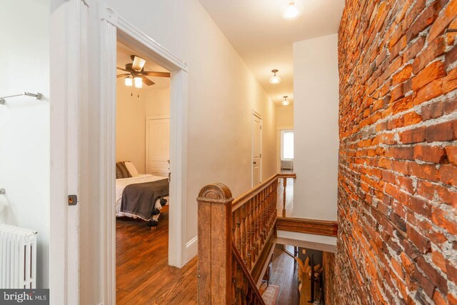 hallway featuring brick wall, an upstairs landing, wood finished floors, and radiator