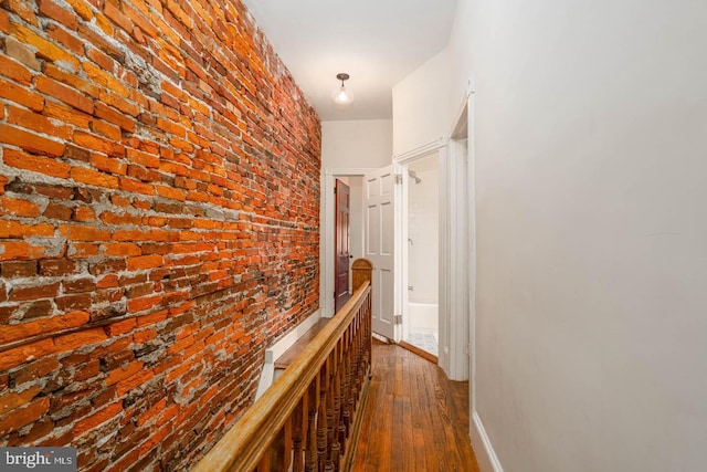 corridor featuring brick wall, dark wood-style floors, and baseboards