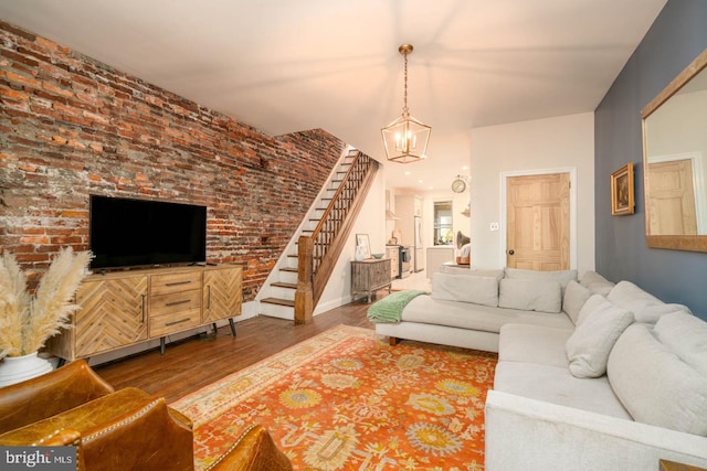 living area featuring brick wall, a chandelier, stairs, baseboards, and wood finished floors