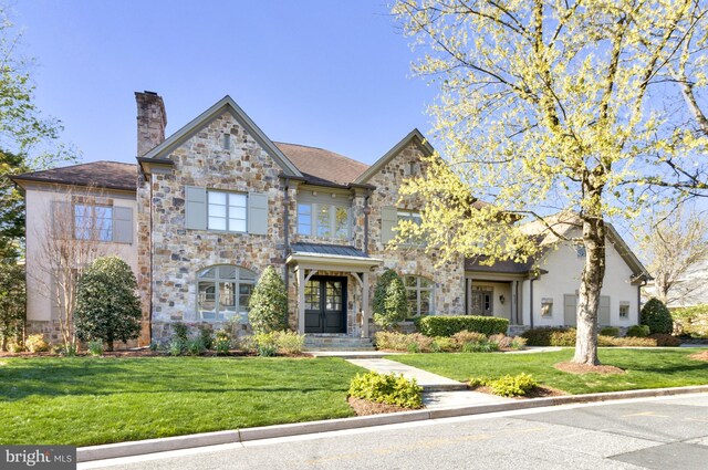 view of front of home with a chimney, stone siding, and a front lawn