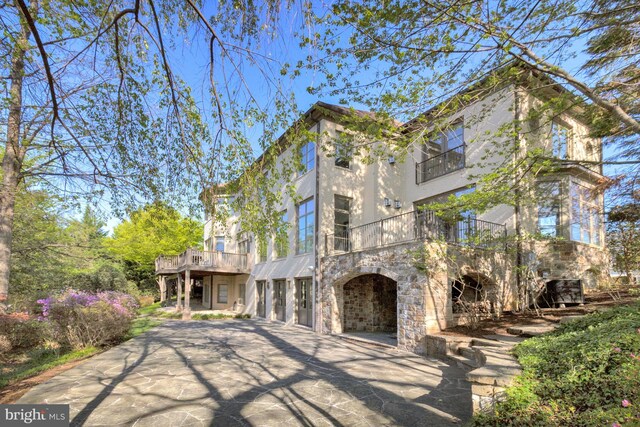 back of property with an attached garage, a balcony, driveway, and stone siding