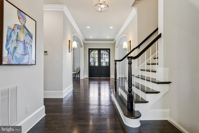 foyer entrance featuring arched walkways, baseboards, ornamental molding, and wood finished floors