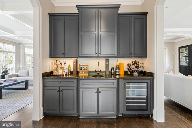 bar featuring crown molding, beverage cooler, indoor wet bar, arched walkways, and a sink