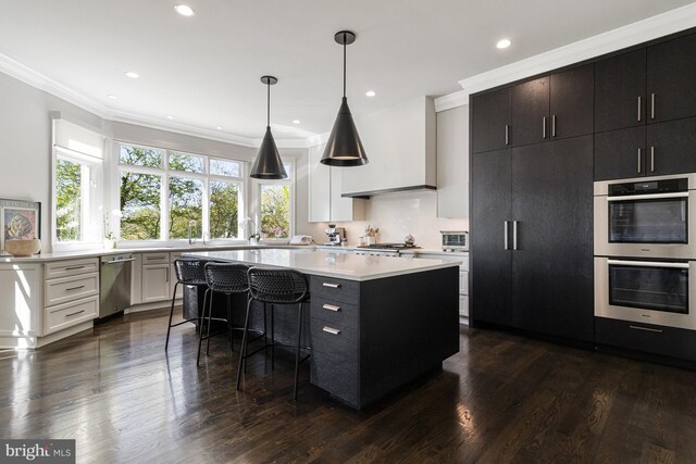 kitchen with crown molding, a kitchen island, dark wood-type flooring, light countertops, and stainless steel appliances
