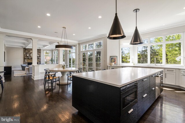 kitchen with crown molding, ornate columns, light countertops, a center island, and dark cabinetry