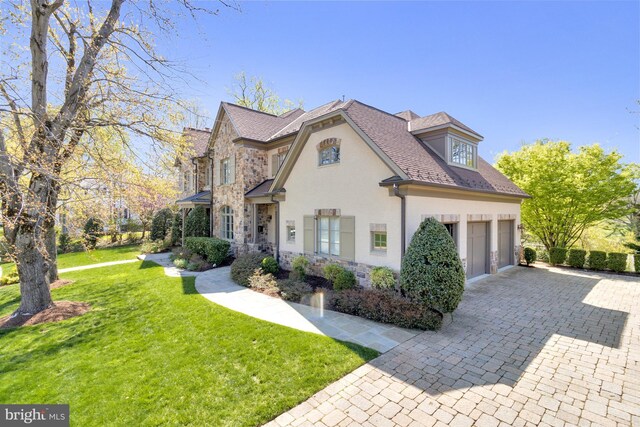 view of front of home featuring a garage, stone siding, a front yard, decorative driveway, and stucco siding