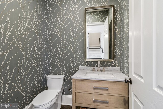 bathroom with vanity, wood finished floors, toilet, baseboards, and wallpapered walls