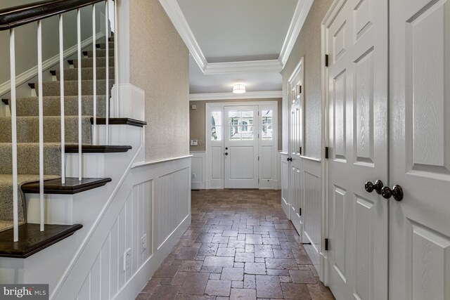 doorway featuring a decorative wall, a wainscoted wall, stone tile floors, ornamental molding, and stairway